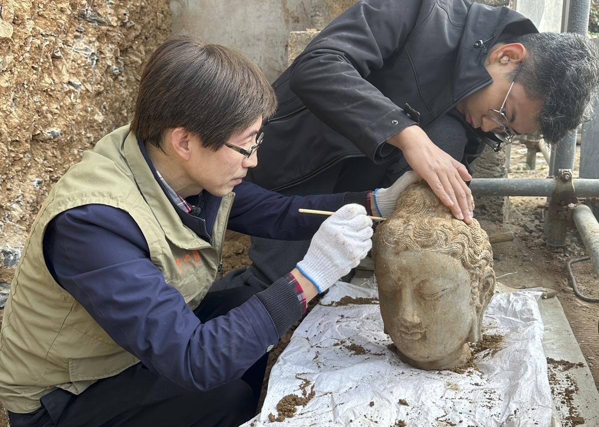 Các nhà khảo cổ làm sạch đầu tượng Phật bằng đá được phát hiện tại hang Leigutai, thuộc quần thể hang Long Môn. Ảnh: China Daily