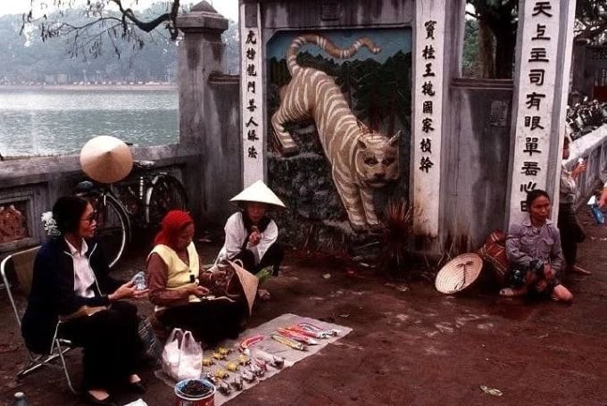 Quầy hàng xén ở đền Ngọc Sơn bày bán con khắc dấu và đồ chơi bằng xốp, giấy cho trẻ em. Phía sau là bức phù điêu hình hổ, tượng trưng cho bảng vàng ghi danh các sĩ tử thi đỗ Tiến sĩ.